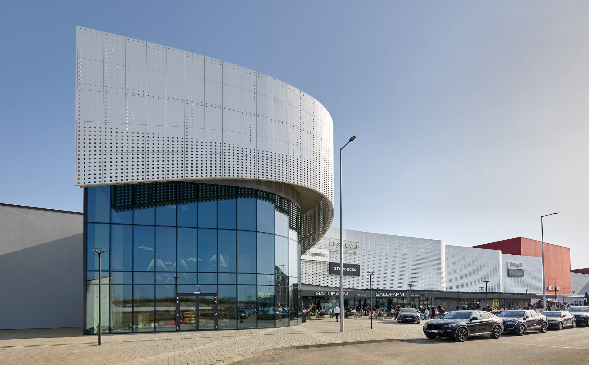 Colțul curbat al volumului alb al Arena Mall Bacău, lângă parcare